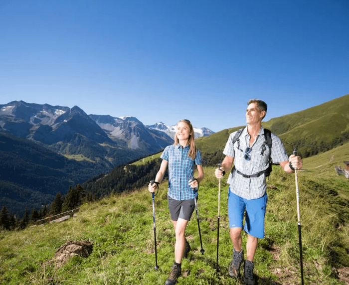 Wanderpaar genießt Sonnenschein in den Zillertaler Alpen – Wandern mit Ausblick auf grüne Berghänge und verschneite Gipfel.